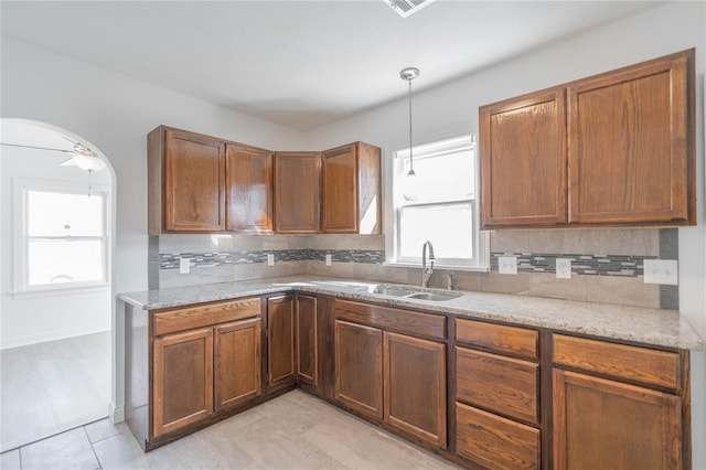 kitchen with light stone counters, decorative light fixtures, sink, and tasteful backsplash