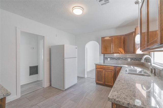 kitchen with tasteful backsplash, light stone countertops, white fridge, and sink