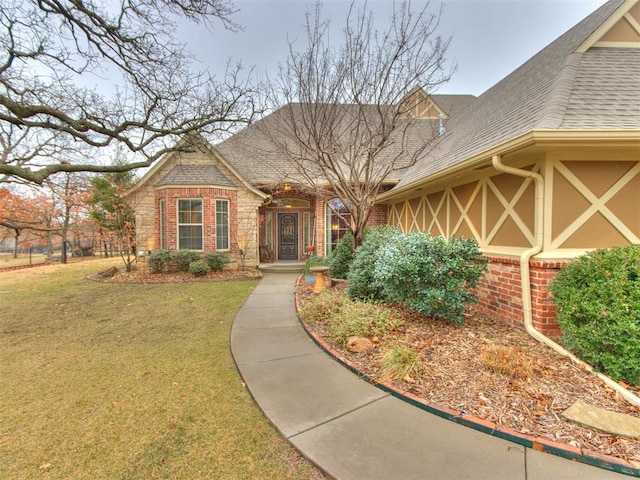 view of front of home with brick siding, a front yard, and a shingled roof