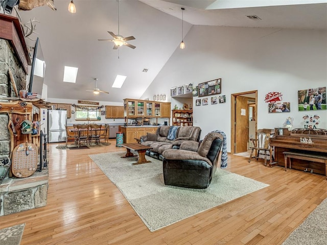 living room with high vaulted ceiling, light hardwood / wood-style flooring, ceiling fan, and a skylight