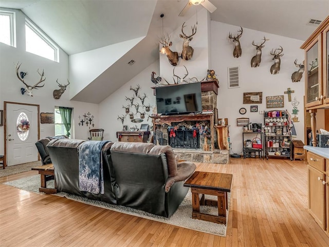 living room with high vaulted ceiling, a fireplace, and light hardwood / wood-style flooring