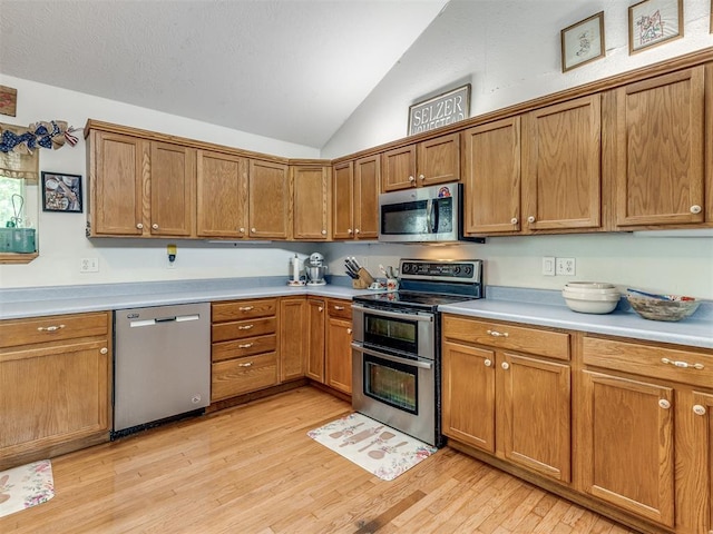 kitchen with appliances with stainless steel finishes, light hardwood / wood-style floors, and vaulted ceiling