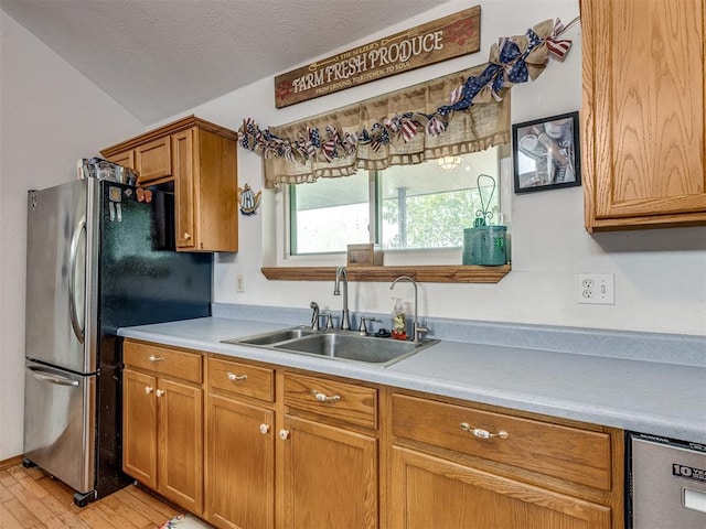 kitchen featuring dishwashing machine, sink, stainless steel refrigerator, light hardwood / wood-style floors, and a textured ceiling