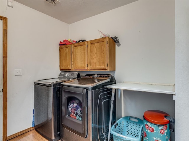 washroom featuring cabinets, washer and clothes dryer, and light hardwood / wood-style flooring