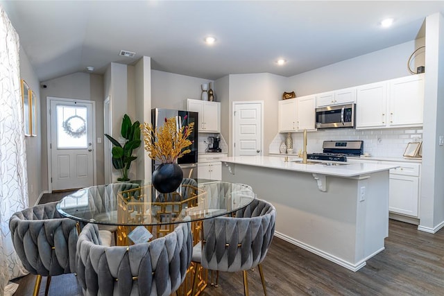 kitchen featuring stainless steel appliances, white cabinetry, dark hardwood / wood-style floors, and a center island with sink