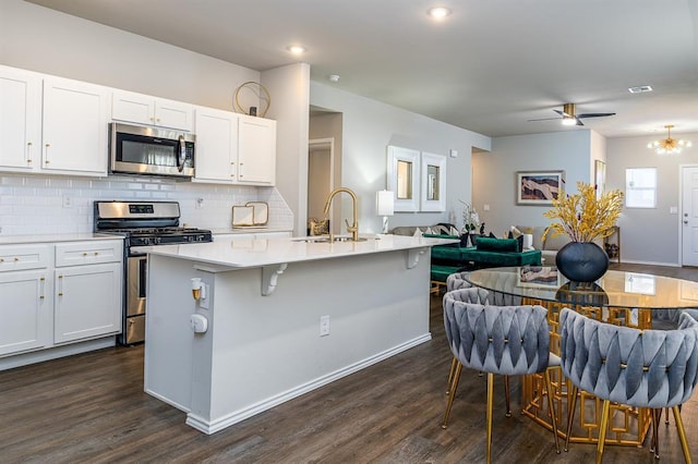 kitchen with a breakfast bar area, dark hardwood / wood-style flooring, stainless steel appliances, a kitchen island with sink, and white cabinets