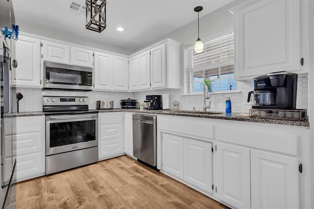 kitchen with light hardwood / wood-style flooring, dark stone counters, white cabinets, and appliances with stainless steel finishes