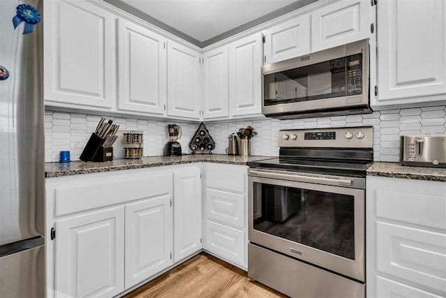 kitchen with white cabinetry, stainless steel appliances, tasteful backsplash, and dark stone counters