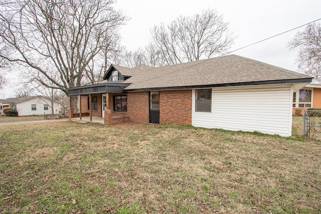 back of house featuring brick siding, a shingled roof, a lawn, a patio area, and fence