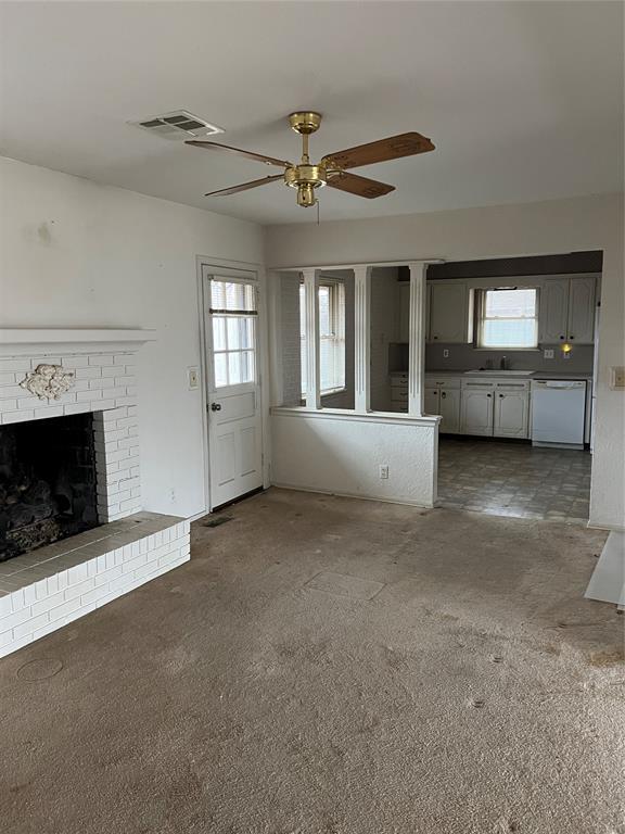 unfurnished living room with a brick fireplace, dark carpet, sink, and ceiling fan