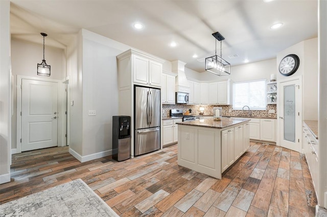 kitchen with sink, appliances with stainless steel finishes, hanging light fixtures, white cabinets, and a kitchen island