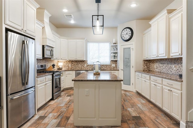 kitchen featuring stainless steel appliances, white cabinetry, a center island, and dark stone counters