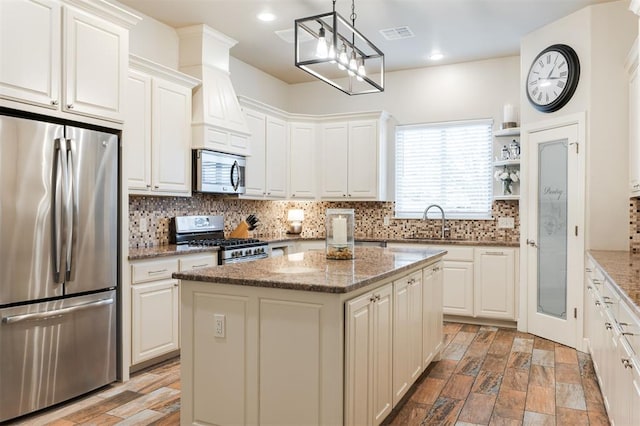 kitchen featuring decorative light fixtures, a center island, stainless steel appliances, light stone countertops, and white cabinets