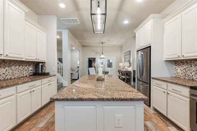 kitchen featuring white cabinetry, dark stone countertops, stainless steel refrigerator, a kitchen island, and pendant lighting