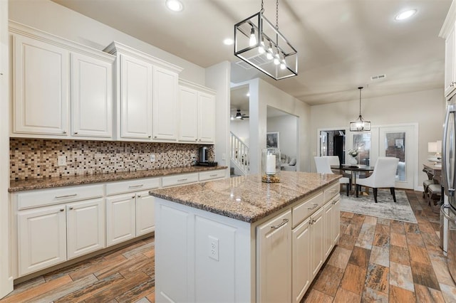 kitchen featuring white cabinetry, decorative light fixtures, light stone countertops, and a center island