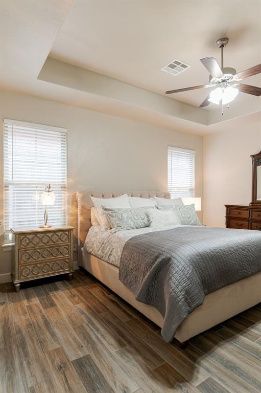 bedroom with dark hardwood / wood-style floors, ceiling fan, and a tray ceiling