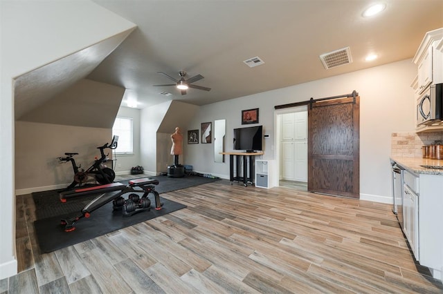 workout room featuring lofted ceiling, light hardwood / wood-style flooring, a barn door, and ceiling fan