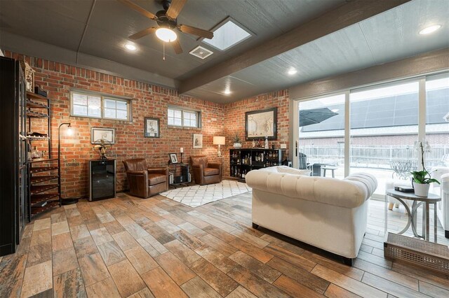 living room featuring beamed ceiling, ceiling fan, brick wall, and light hardwood / wood-style flooring