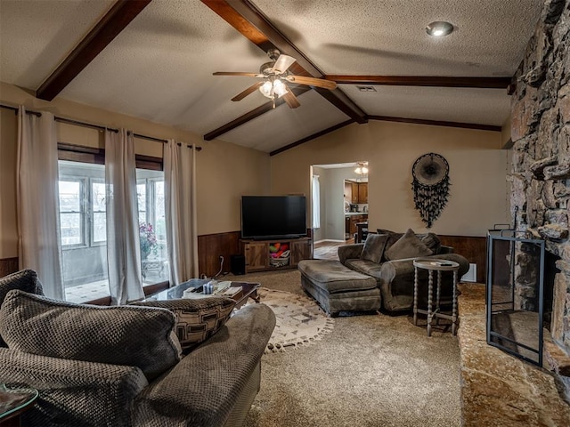 carpeted living room with ceiling fan, wooden walls, lofted ceiling with beams, a textured ceiling, and a stone fireplace