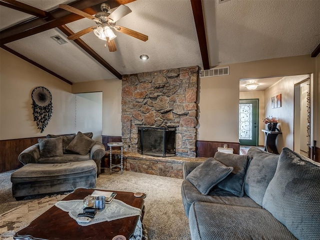 carpeted living room featuring lofted ceiling with beams, a stone fireplace, wooden walls, and a textured ceiling