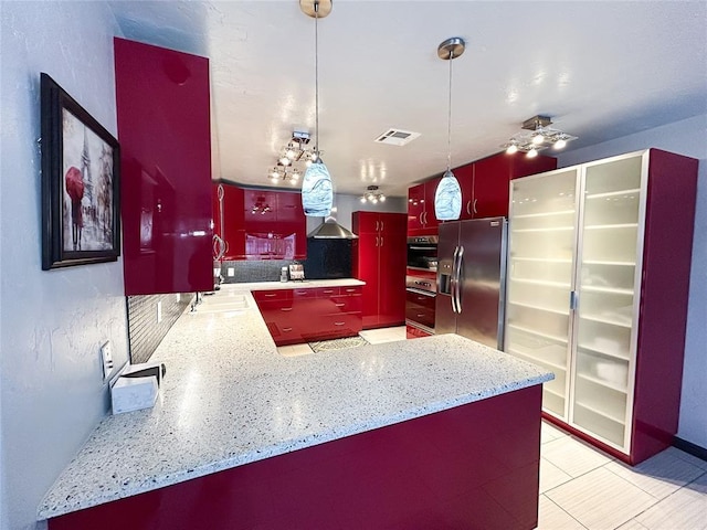 kitchen with sink, appliances with stainless steel finishes, kitchen peninsula, pendant lighting, and light stone countertops