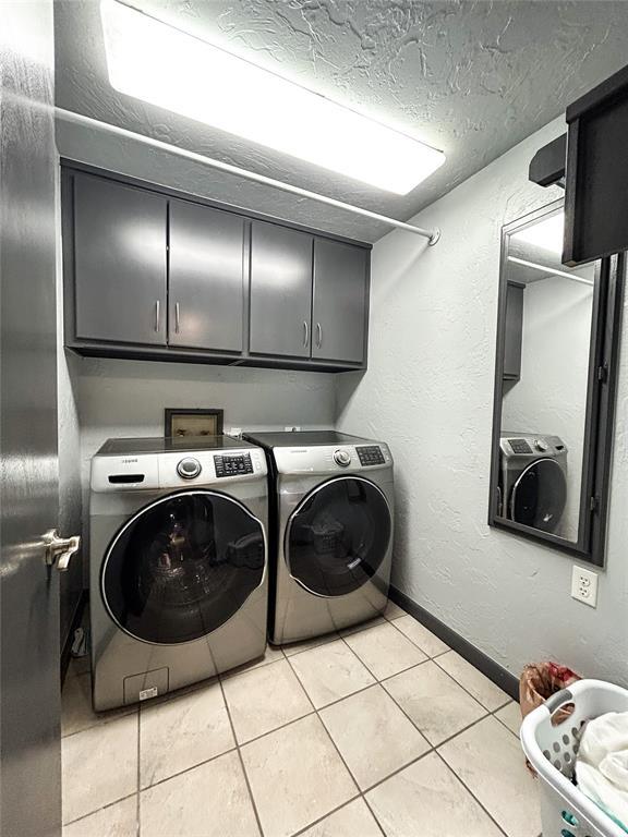 laundry room with cabinets, washing machine and dryer, a textured ceiling, and light tile patterned floors