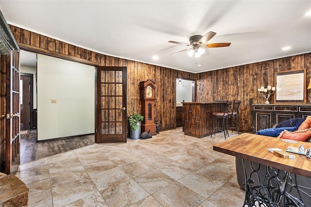 living room with ceiling fan, indoor bar, and wooden walls