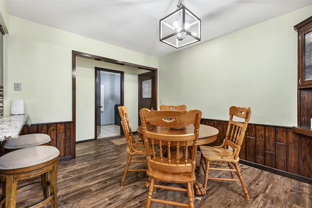 dining space with dark wood-type flooring, a chandelier, and wooden walls