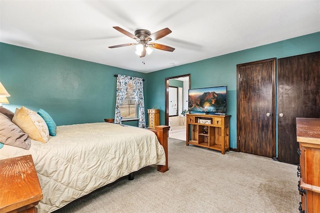 bedroom featuring ceiling fan, light colored carpet, and ensuite bath