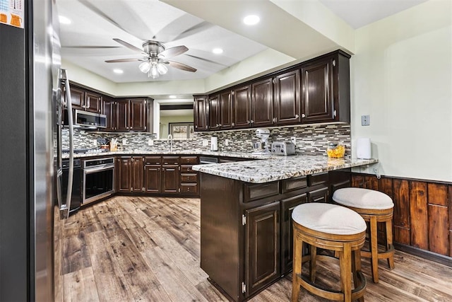 kitchen featuring light hardwood / wood-style flooring, appliances with stainless steel finishes, backsplash, dark brown cabinetry, and kitchen peninsula