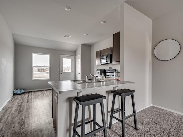kitchen with sink, a kitchen bar, kitchen peninsula, dark brown cabinets, and stainless steel range oven
