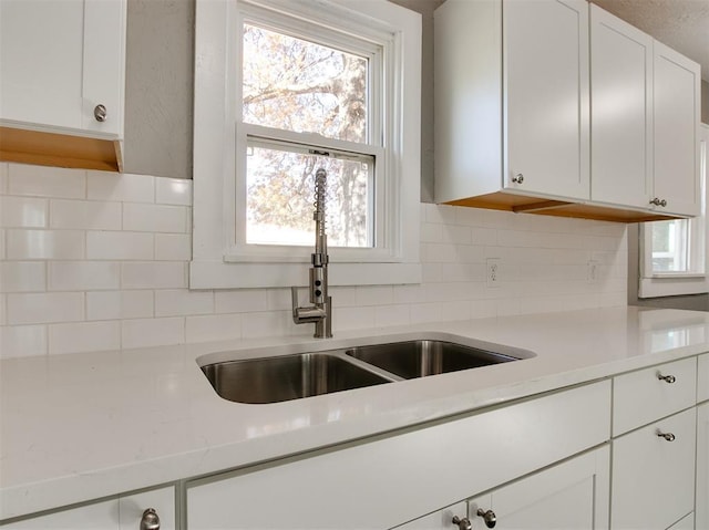 kitchen featuring tasteful backsplash, sink, white cabinets, and light stone counters