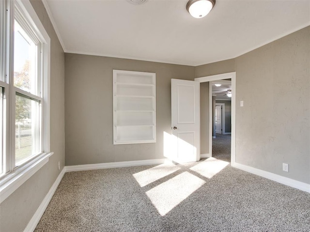 carpeted empty room with built in shelves, ornamental molding, and a healthy amount of sunlight