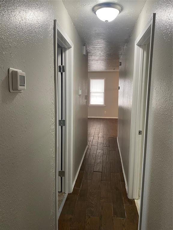 hallway with a textured ceiling and dark hardwood / wood-style flooring