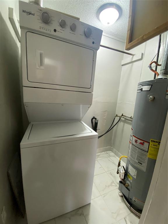 laundry room featuring stacked washer / drying machine, water heater, and a textured ceiling