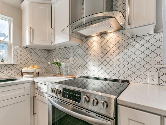 kitchen featuring white cabinetry, stainless steel electric stove, backsplash, and wall chimney exhaust hood