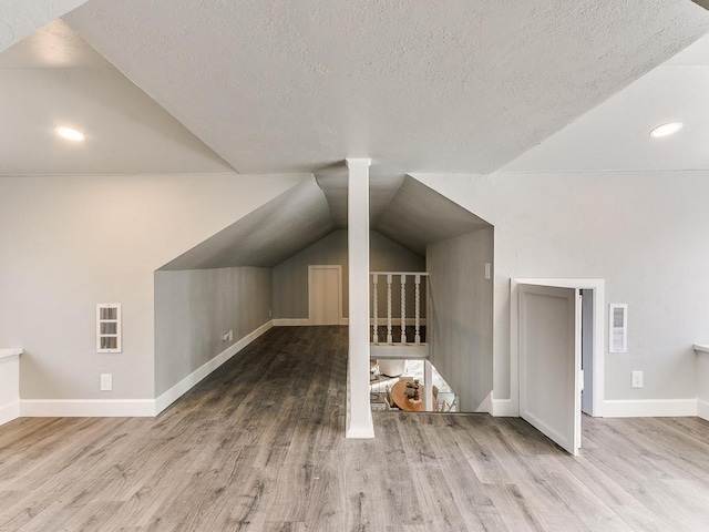 bonus room with vaulted ceiling, a textured ceiling, and light wood-type flooring