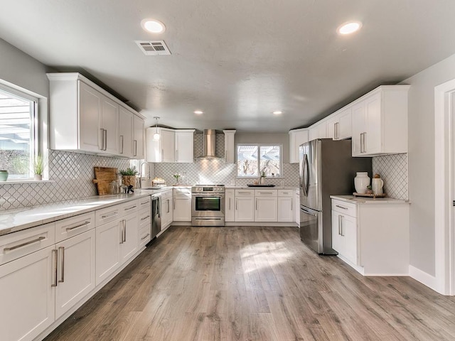 kitchen with appliances with stainless steel finishes, sink, white cabinets, light hardwood / wood-style floors, and wall chimney exhaust hood