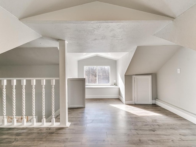 additional living space with hardwood / wood-style flooring, lofted ceiling, and a textured ceiling