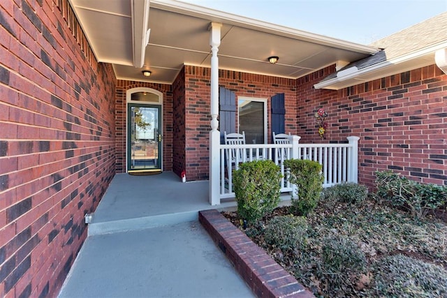 view of exterior entry with a porch and brick siding