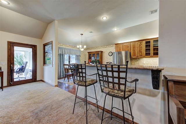 kitchen featuring carpet floors, visible vents, vaulted ceiling, freestanding refrigerator, and brown cabinets