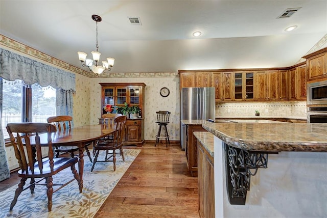 kitchen featuring stainless steel appliances, stone countertops, visible vents, and brown cabinets