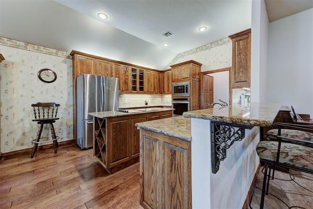 kitchen featuring light wood-style flooring, stainless steel appliances, a peninsula, visible vents, and brown cabinets