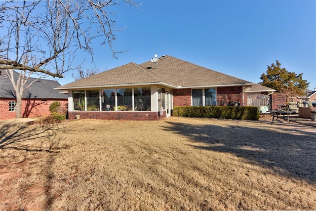 rear view of house featuring a sunroom, brick siding, a lawn, and roof with shingles