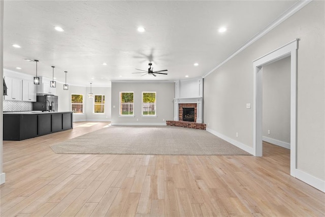 unfurnished living room featuring ceiling fan, ornamental molding, a fireplace, and light wood-type flooring