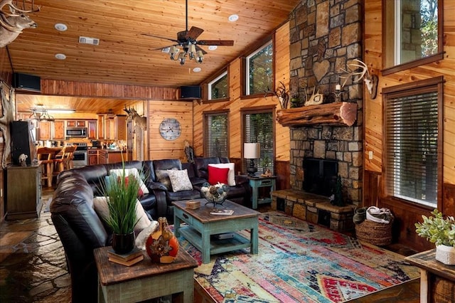 living room featuring wood walls, wooden ceiling, ceiling fan, a towering ceiling, and a fireplace