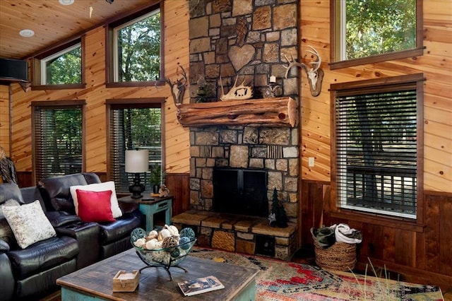 living room featuring wood ceiling, a towering ceiling, a stone fireplace, and wood walls