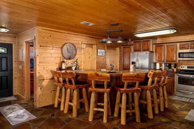 kitchen featuring appliances with stainless steel finishes, wooden walls, a kitchen bar, and wooden ceiling