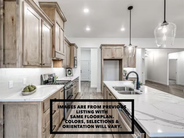 kitchen with sink, hanging light fixtures, stainless steel range with gas stovetop, light stone countertops, and an island with sink