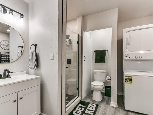 bathroom with hardwood / wood-style floors, vanity, stacked washer / drying machine, walk in shower, and toilet